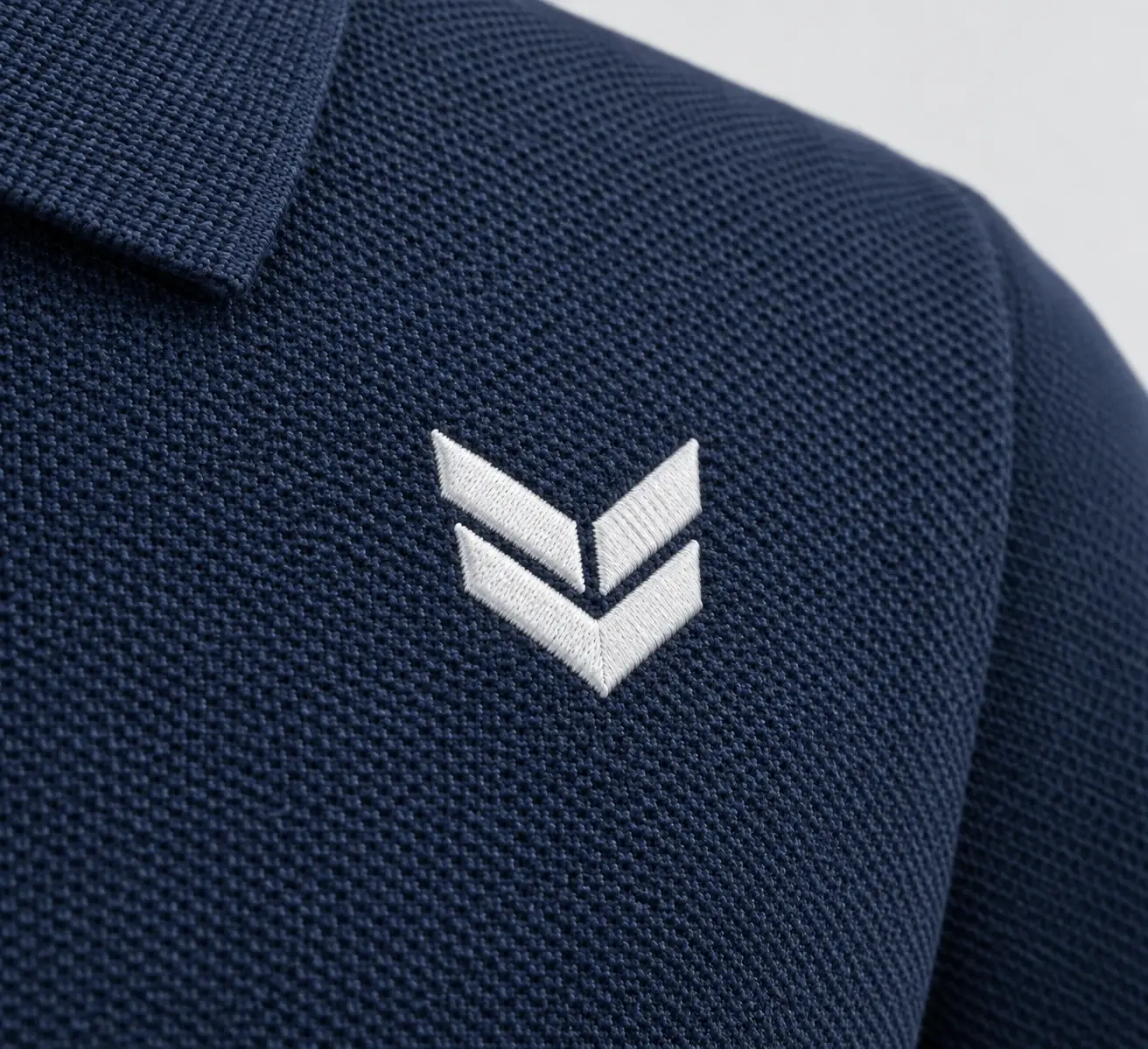Logo chevron brodé en blanc sur un piqué marine, vu en macro.